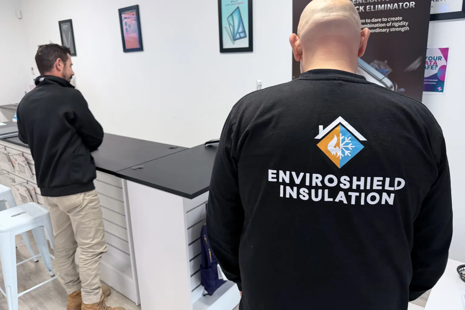 An EnviroShield Insulation team member in a branded shirt at the EduCom IT Albury service counter, talking with an EduCom IT technician.
