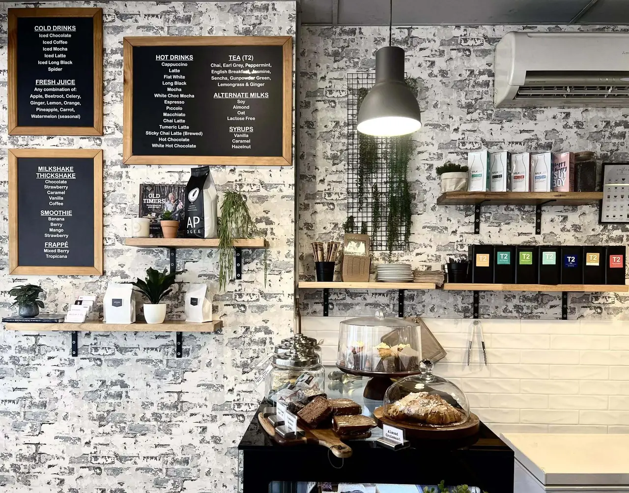 The menu boards above the Willow & Co. counter, listing hot drinks, teas, alternate milks, syrups, milkshakes and juices beside the pastry cabinet.